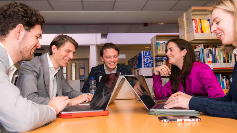 Two master students discuss a project with a lecturer in one of the hotel school corridors.