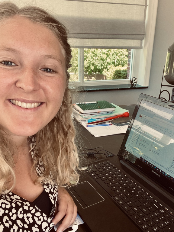 Merel Nijsten Master FREM student sitting behind her laptop taking a selfie. wearing a black and white shirt. girl has blond hair and blue eyes and smiles