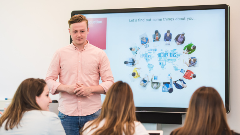 Student stands in front of the smart board in the classroom and gives presentation to his fellow students at the hotel school maastricht.